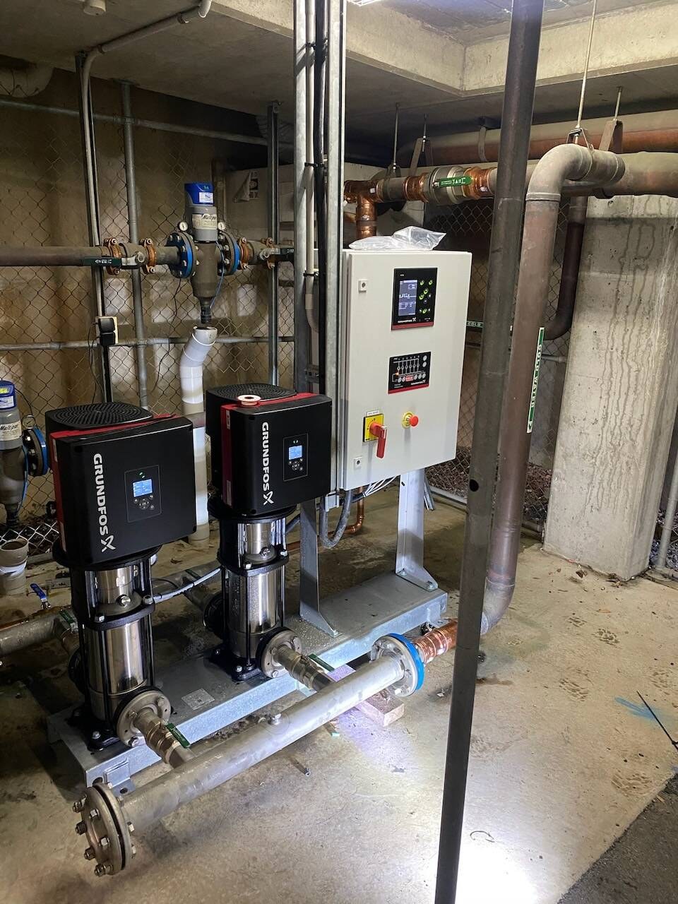Booster pumps, control panel and pipework in a plant room