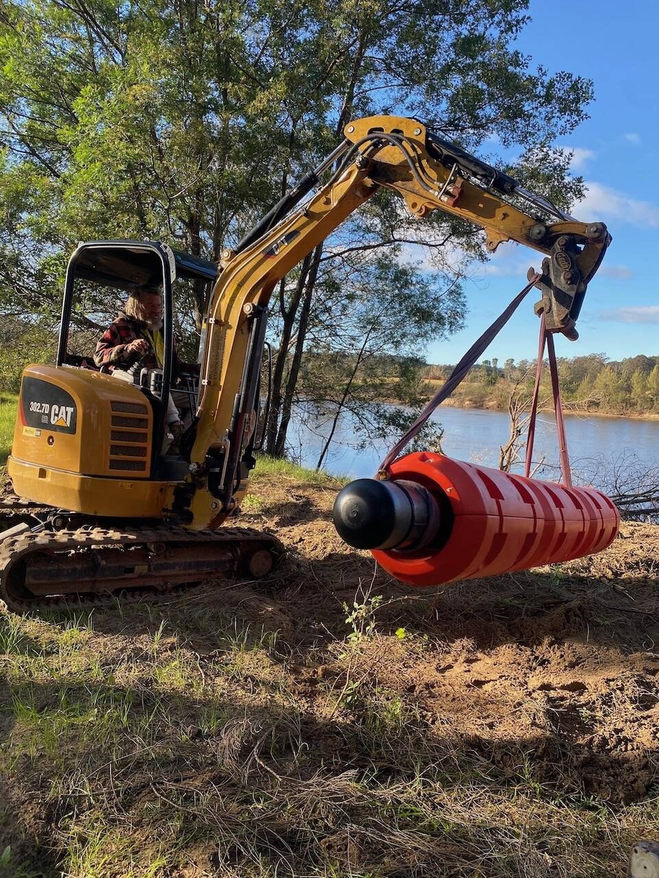 Mini excavator lifting a float pump beside the river